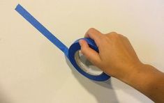 a person using a blue tape to attach a wall mounted toilet paper dispenser