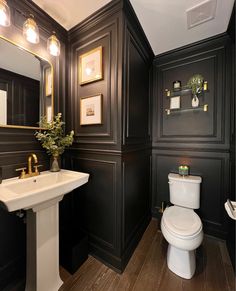 a white toilet sitting next to a sink in a bathroom under two framed pictures on the wall