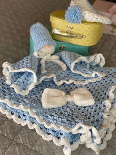 a crocheted baby blanket and booties sitting on a bed next to a suitcase