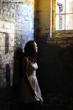 a woman standing in front of a brick wall with her head turned to the side