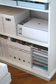 a white shelf filled with files and computer equipment on top of a hard wood floor