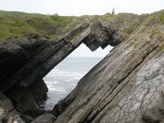 a man standing on top of a rocky cliff next to the ocean with an opening in it