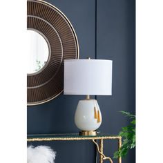 a white and gold lamp sitting on top of a table next to a round mirror