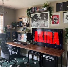 a desk with two computers on it in front of some pictures and other things hanging on the wall