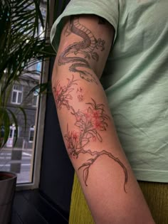 a person with a dragon tattoo on their arm next to a potted plant and window