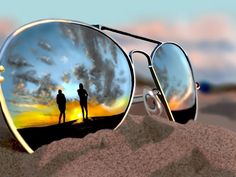 the reflection of two people in sunglasses is shown on top of a sand dune at sunset