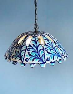 a blue and white lamp hanging from a chain on a light fixture against a blue sky