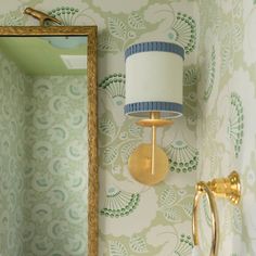 a bathroom with green and white wallpaper, gold fixtures and a mirror on the wall