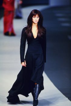 a woman is walking down the runway in a long black dress and knee high boots