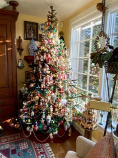 a brightly colored christmas tree is in the corner of a living room with a large window