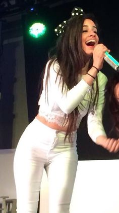 two women in white outfits singing into microphones at a music event with green lights behind them