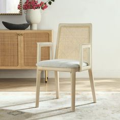 a white chair sitting in front of a mirror on top of a wooden dresser next to a vase with flowers