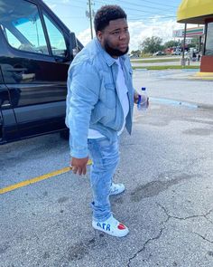 a man standing in the middle of a parking lot next to a blue truck and holding a cup