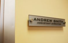 a sign on the wall that says andrew smith assistant director in black lettering,