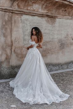 a woman in a white wedding dress standing against a stone wall with her back to the camera