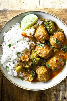 a white plate topped with meatballs, rice and broccoli next to a pickle