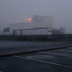 an empty parking lot in front of a large factory building on a foggy day