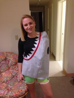 a woman standing in front of a bed with a shark sweater over her shoulders and green shorts