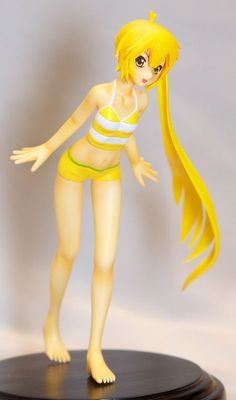 a plastic doll is posed on a black base with a white and yellow striped top