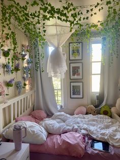 an unmade bed with white sheets and pink comforter in a bedroom decorated with ivy vines