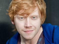 a close up of a person with red hair and blue shirt smiling at the camera