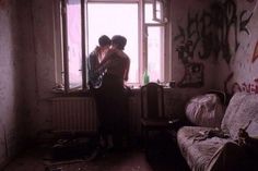 two people standing in front of a window with graffiti on the walls and windowsill