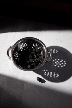 a metal strainer filled with blackberries on top of a table