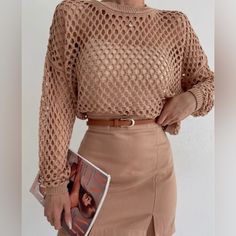 a woman is holding a magazine and wearing a brown top with crochet on it