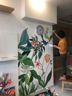 a woman is painting a wall with flowers and birds on it in the kitchen area