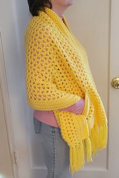 a woman standing in front of a door wearing a yellow knitted shawl with fringes