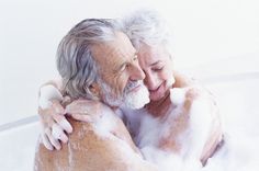 an older man and woman are hugging in the bathtub with foam on their backs