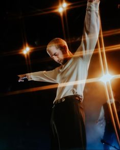 a man in white shirt and black pants on stage with arms raised above his head