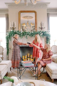 three women sitting in front of a fire place with candles on the mantels