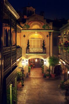 the entrance to an apartment building at night with lights on and potted plants outside