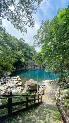 the blue lake is surrounded by green trees and rocks, with a wooden walkway leading to it