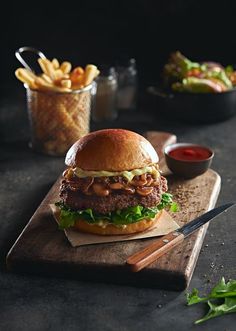 a large hamburger sitting on top of a cutting board next to french fries and ketchup