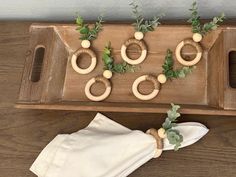 a wooden tray with green plants and rings on it, sitting next to a napkin holder