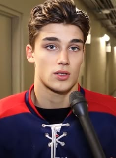 a young man holding a microphone in his hand and wearing a red, white and blue jacket