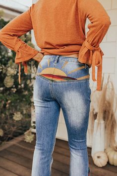 the back of a woman's jeans, with her hands on her hips and wearing an orange sweater