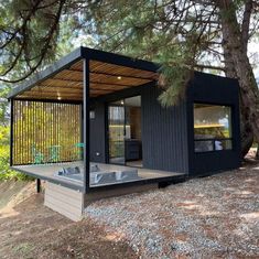 a small black cabin in the woods with a hot tub under it's roof