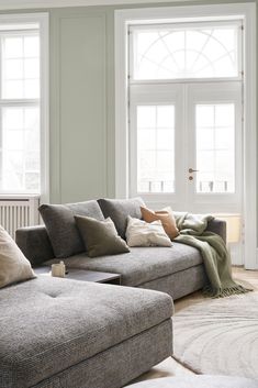 a living room filled with lots of furniture next to two windows and a rug on the floor