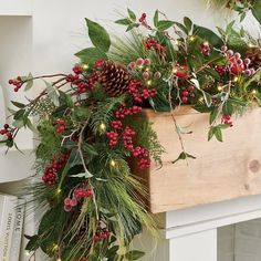 a wooden box filled with greenery and red berries on top of a mantel