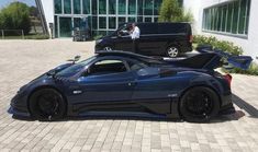 a blue sports car is parked in front of a building with two people standing next to it