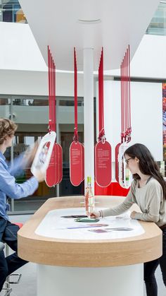 two people are sitting at a table with red tags hanging from the ceiling