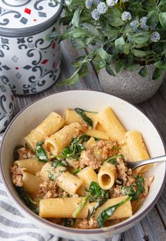 a white bowl filled with pasta and spinach on top of a table next to a potted plant