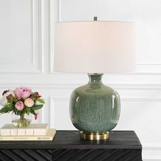 a green vase sitting on top of a table next to a lamp and bookend