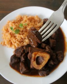 a fork is stuck into some food on a plate with rice and meat in gravy