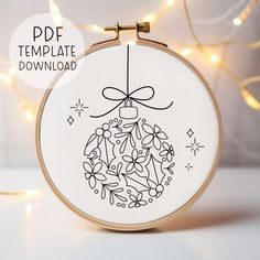 a cross stitch christmas ornament hanging from a hoop with lights in the background