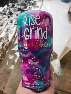 a hand holding up a purple and blue cup with the words rise and grind on it