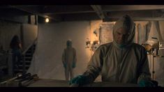 a man in a white coat and blue gloves standing next to a table with some food on it